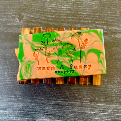 a bar of orange and green cucumber melon soap on a wooden soap dish
