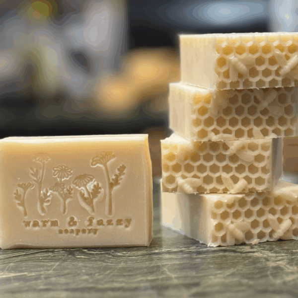 a stack of soap with honeycomb and bumble bee imprints and a single soap with a logo stamped on it