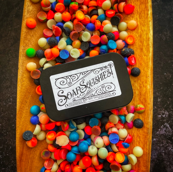 A tin that says soap squishies surrounded by soap squishie son a wood tray