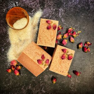 three bars of pink soap with rose buds on each nexts to a small bowl of salt that has spilled