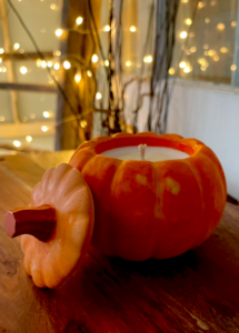 orange pumpkin shaped candle with twinkling lights in the back ground