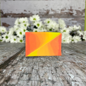 A bar of orange and yellow soap on a wooden table in front of white daisies