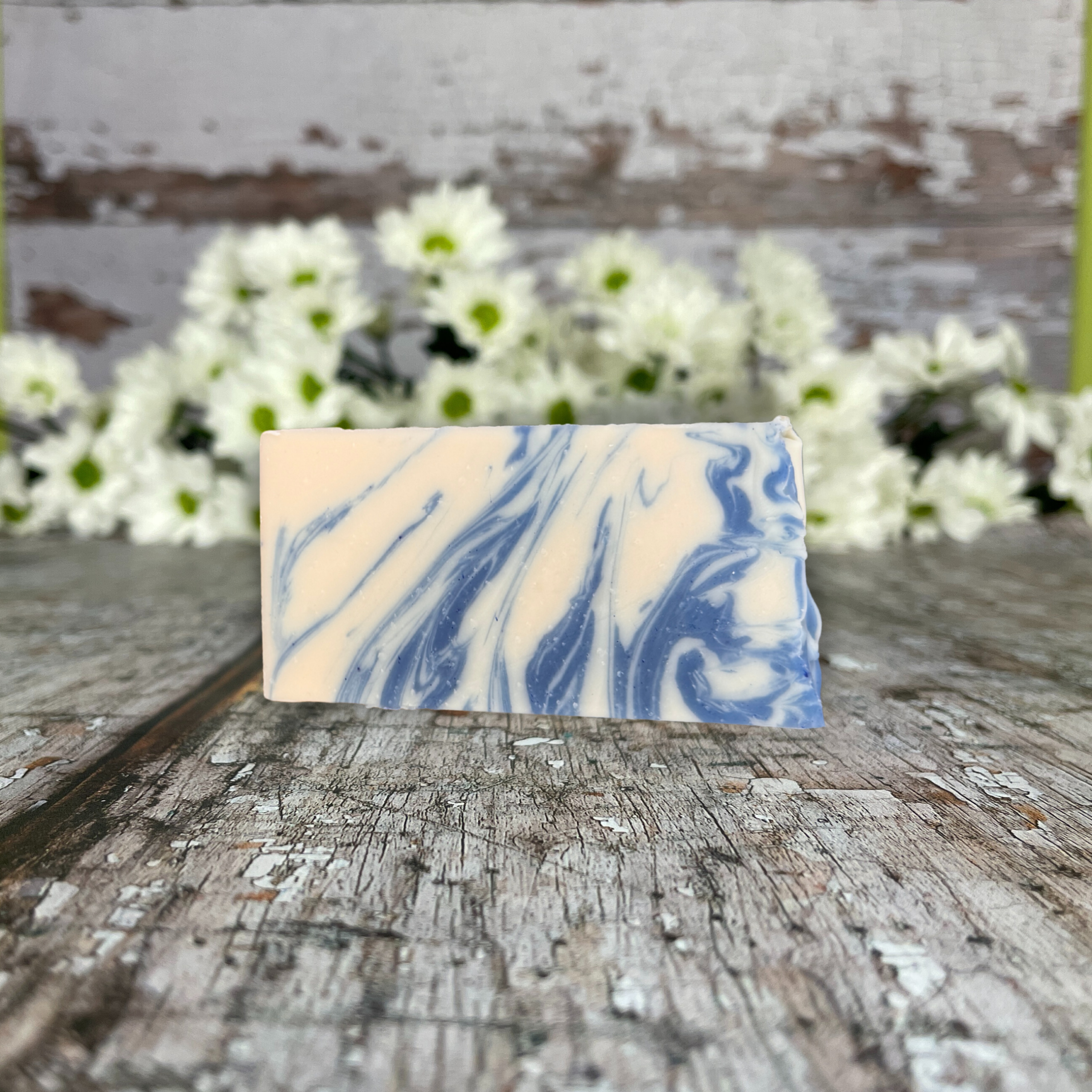 a bar of white and blue soap on a wood table in fron tof white daisies
